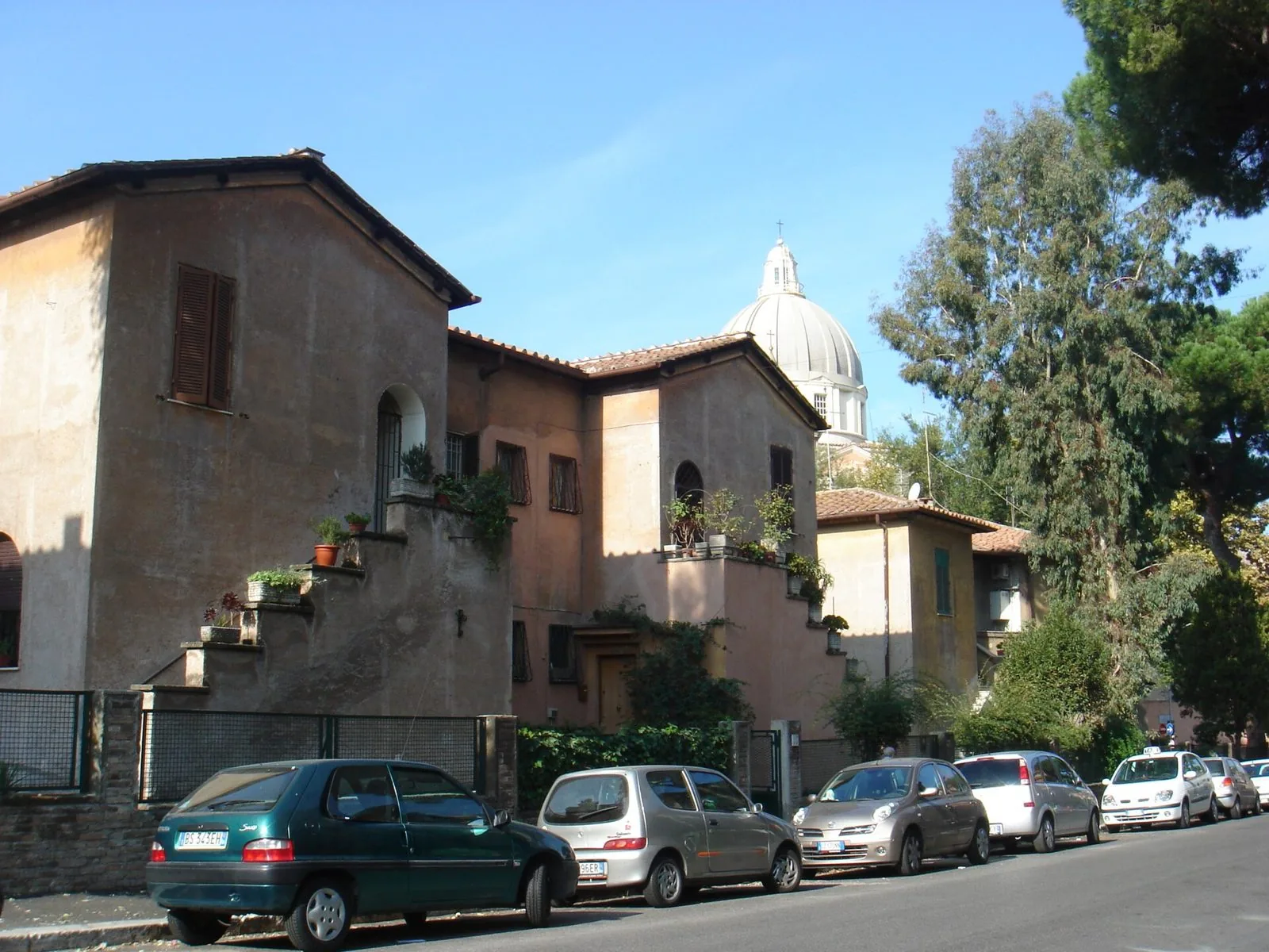 Palazzine storiche della Garbatella con scalette esterne e piante, sullo sfondo una cupola